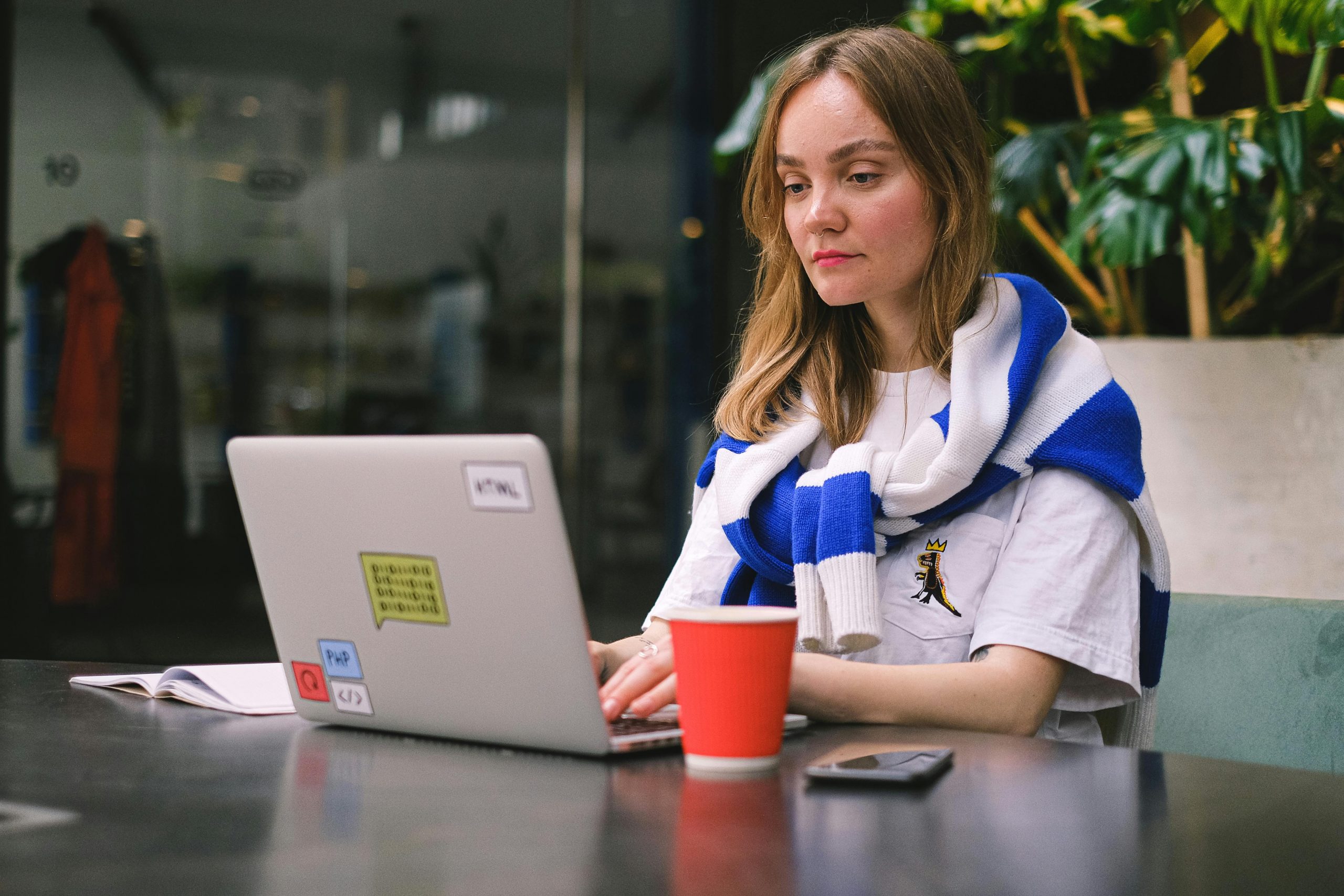 woman working on a laptop with stickers and a cup of coffee beside her